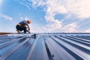 roof construction concept, roofer using air or pneumatic nail gun and installing on new roof metal sheet.