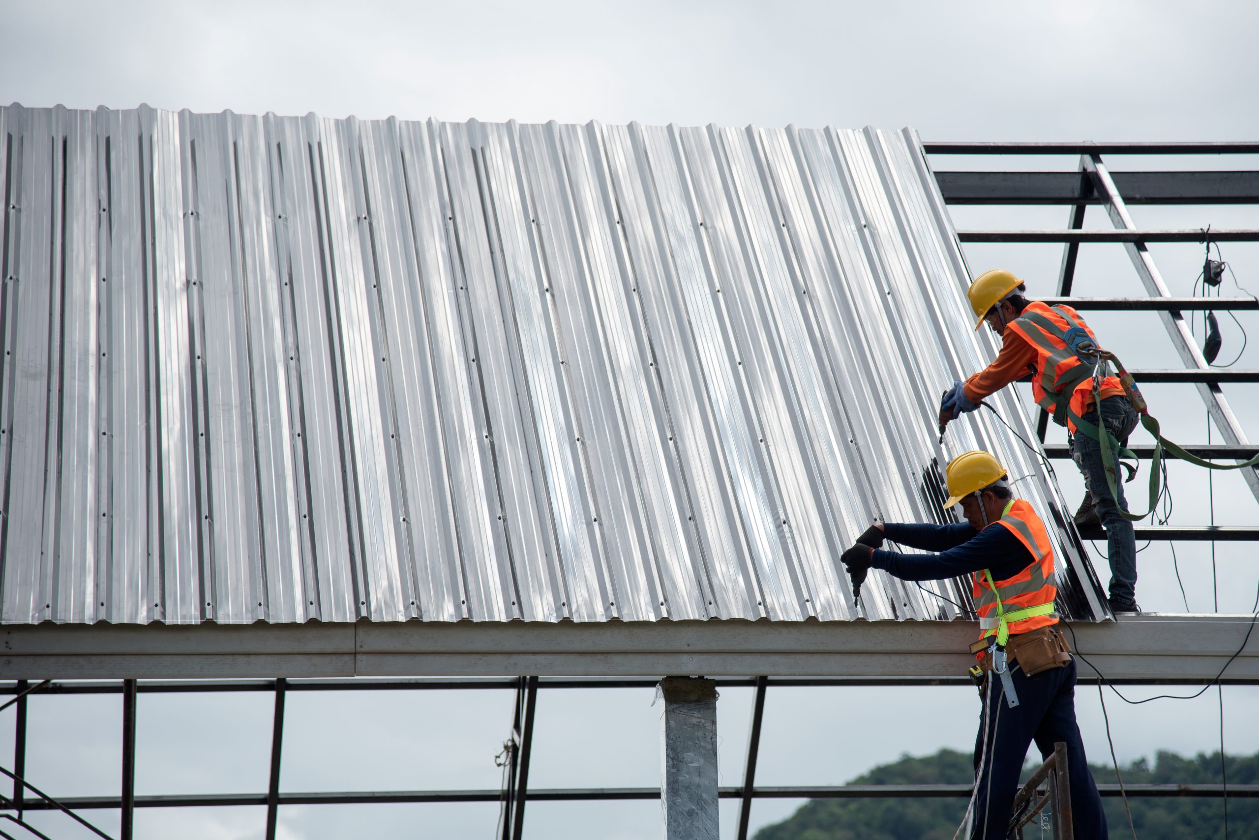 2 workers for construction, installing metal roofing tools, sheet metal new electric drill tool used on a new roof with metal sheets.